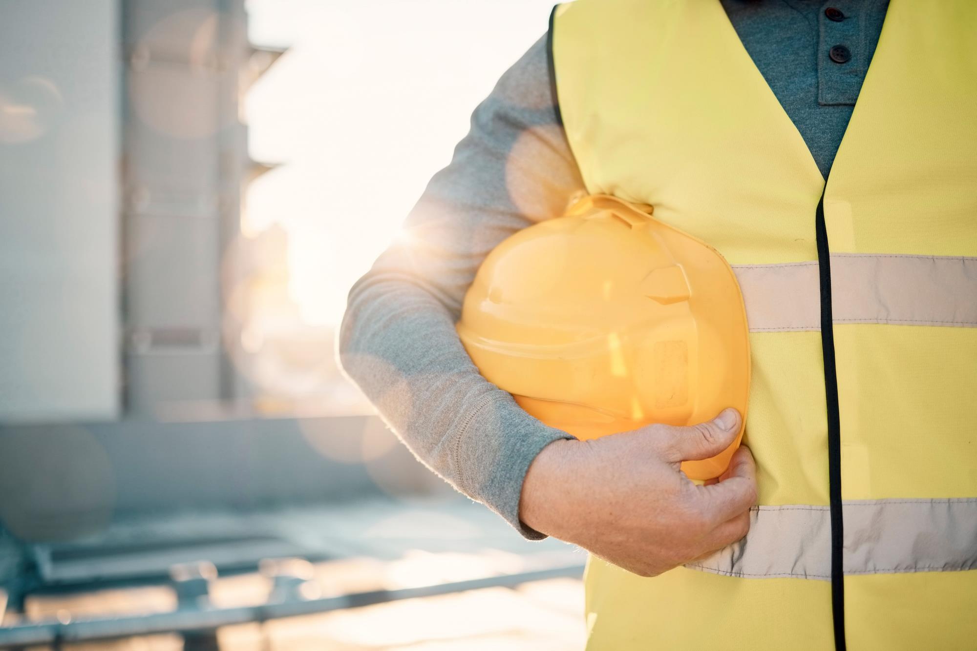 A man with safety vest, holding yellow helmet