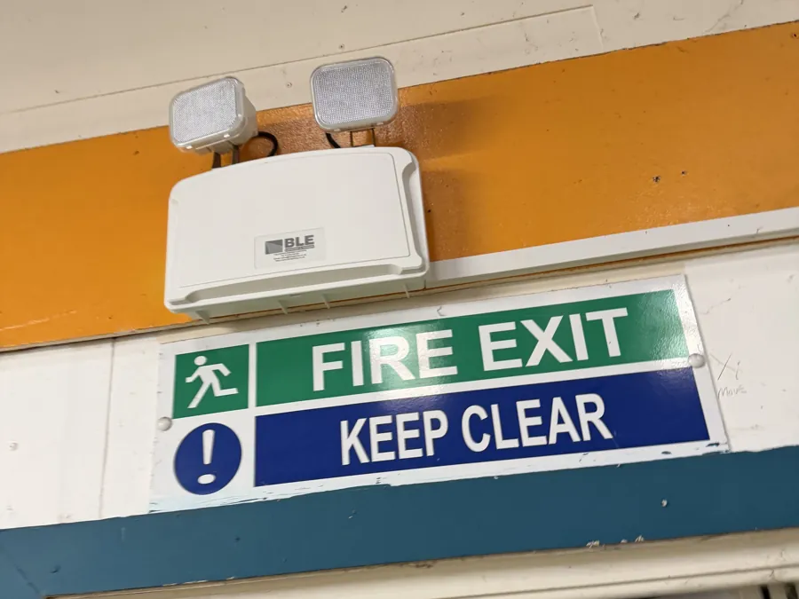 A fire exit keep clear sign and emergency lighting over an exit door